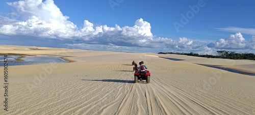 Lençóis Maranhenses. Group of tourists riding quad bikes on an adventurous tour through sand dunes and lagoons. Desert landscape with a blue sky and white clouds. Concept of travel and freedom.