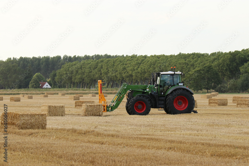 Obraz premium a tractor with a front loader is loading big straw bales in field in the dutch countryside in summer