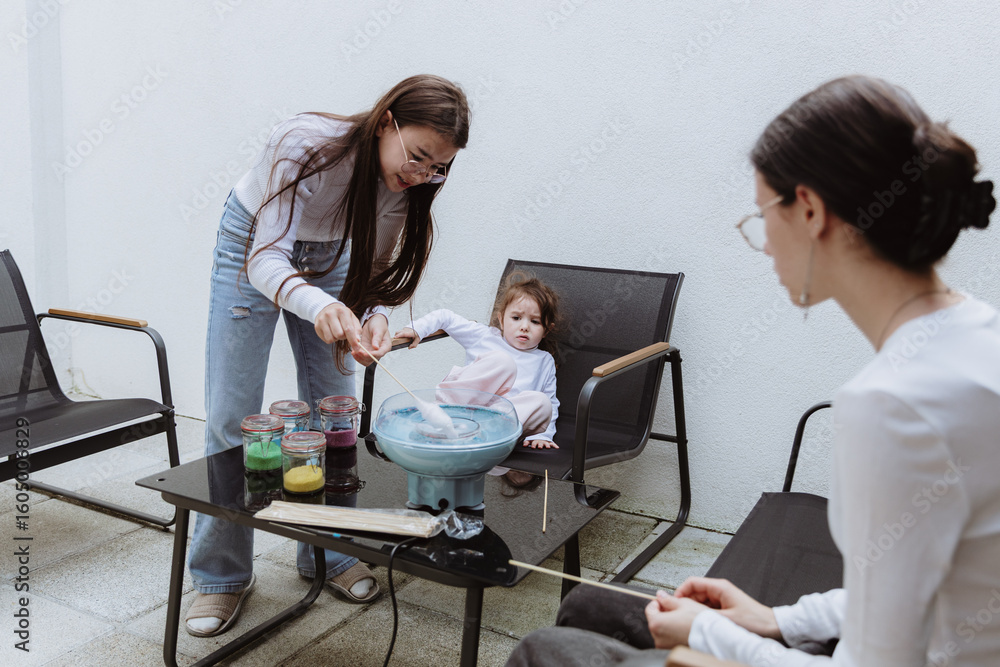 Obraz premium Three cheerful sisters make cotton candy in their backyard.