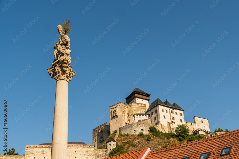 Fototapeta premium Pestsäule zum Gedenken der Opfer der Pest zum Beginn des 18. Jahrhunderts, im Hintergrund ist die Burg Trenčín , Kulturhauptstadt 2026, Trenčín, Slowakei