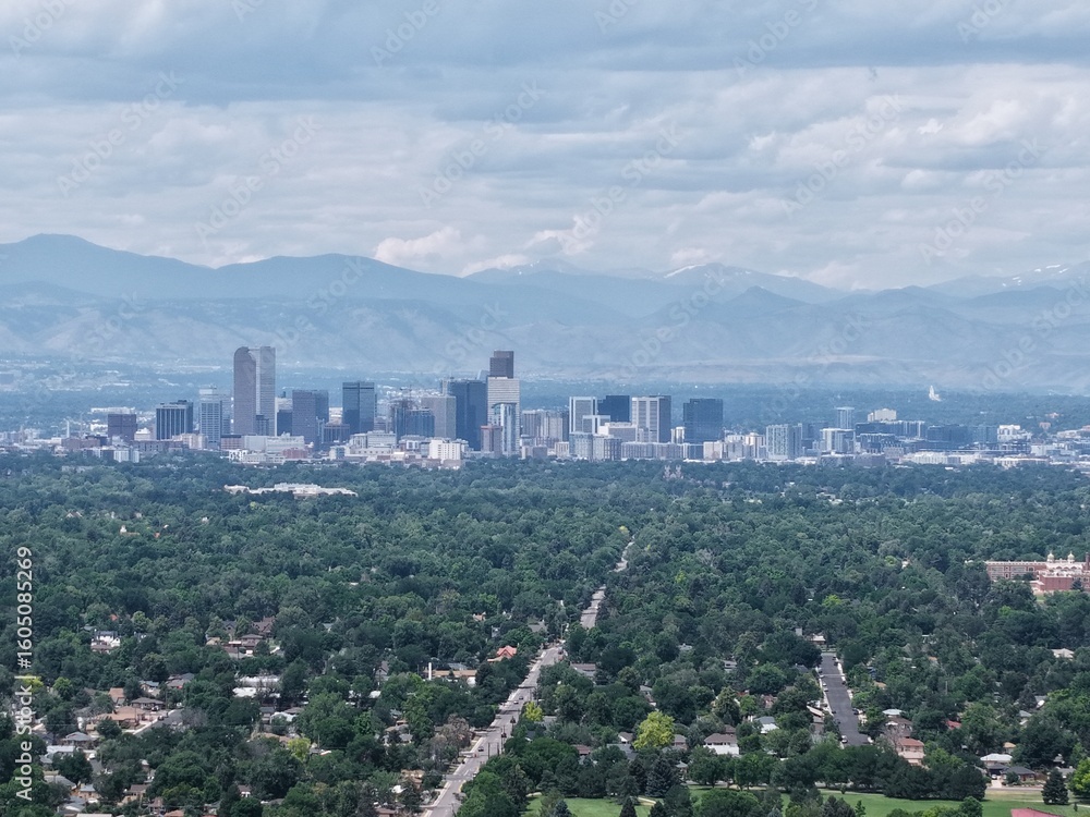 Fototapeta premium Panoramic drone shot: beautiful Denver metropolitan area, lush green urban forest, and dramatic mountain backdrop. Travel and landscape