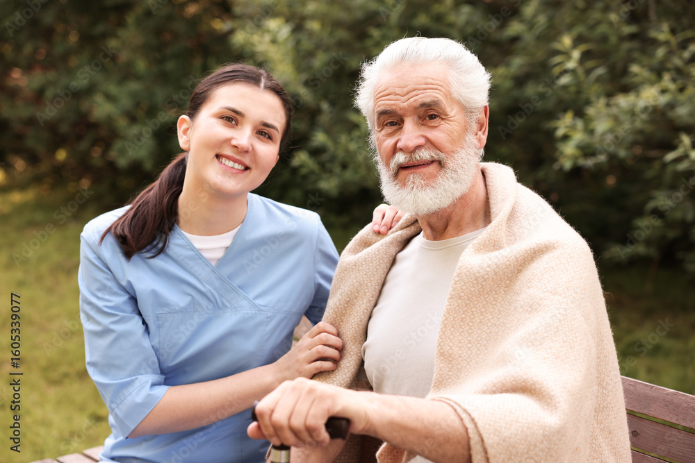 Obraz premium Smiling nurse with elderly man on bench outdoors