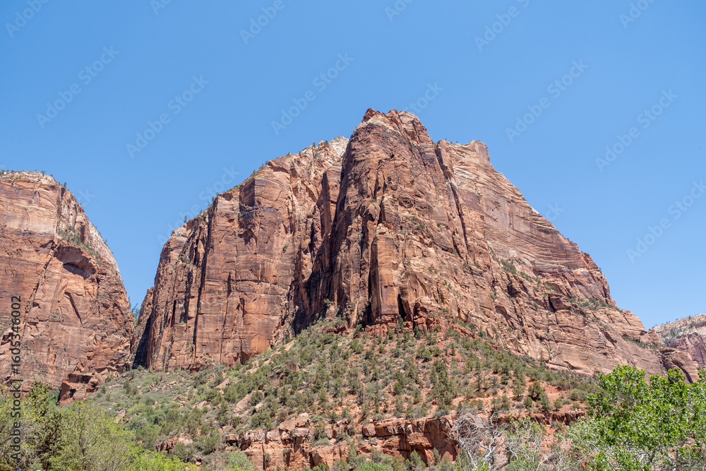 Fototapeta premium The steep, jagged peak of a Zion mountain juts into the sky, highlighted in warm tones under the bright desert sun, Zion, UT