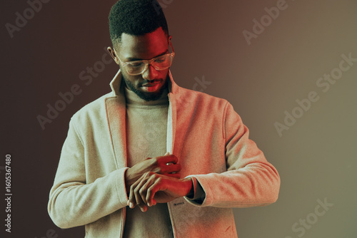 Bilde på lerret Stylish man adjusting his watch, wearing a beige coat and sweater, exuding confi