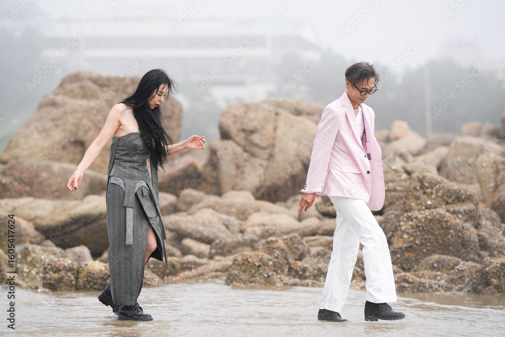 In June 2025, a Korean man and woman in their late fifties are playing together along the rocky shoreline, stepping over jagged stones and enjoying the coastal scenery in Incheon Metropolitan City. In June 2025, a Korean man and woman in their late fifties are playing together along the rocky shoreline, stepping over jagged stones and enjoying the coastal scenery in Incheon Metropolitan City.