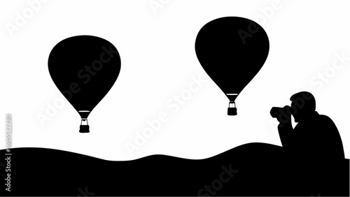 Silhouette of a photographer taking pictures of hot air balloons over a wavy landscape in black and white
