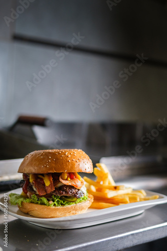 Delicious hamburger with french fries sitting on metal counter in restaurant kitchen