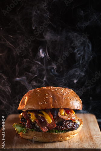 Steaming hot hamburger with bacon and cheese on wooden board