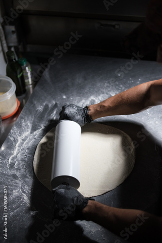 Pizza chef preparing dough with rolling pin in restaurant kitchen