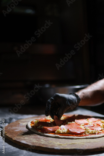 Chef placing pepperoni slices on pizza dough in restaurant kitchen
