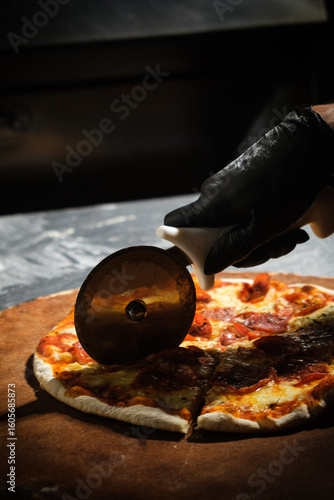 Chef slicing freshly baked pepperoni pizza with pizza cutter