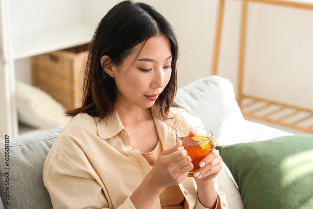 Beautiful young Asian woman with cup of tea in living room Beautiful young Asian woman with cup of tea in living room