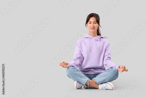 Young woman meditating on light background