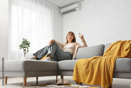 Young woman sitting on sofa near air conditioner at home
