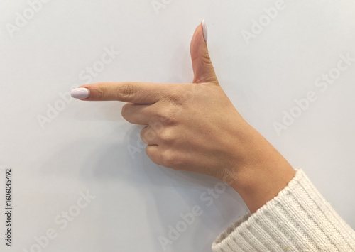 Female hand pointing with gun gesture on white background and soft manicure