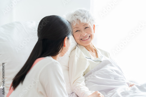 ベッドに寝るシニア女性を介護する介護福祉士