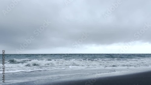 曇り空と白い波が割れる初夏の波打ち際