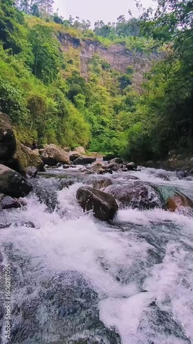 A clear, fast-flowing river cascades over and around numerous large rocks and boulders, creating white water and ripples