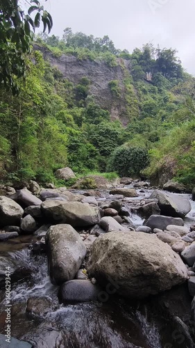 A clear, fast-flowing river cascades over and around numerous large rocks and boulders, creating white water and ripples