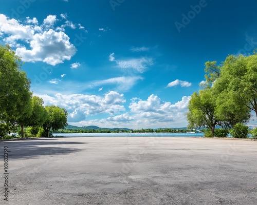 Fototapeta Naklejka Na Ścianę i Meble -  Asphalt Lot, Trees, and Water View under a Partly Cloudy Sky
