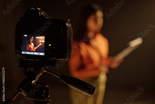 Young adult Hispanic woman standing in front of camera holding script, performing monologue during acting audition, digital camera on tripod recording audition process in studio