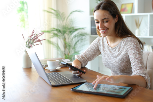 Fotografie Happy woman using multiple devices on a table at home