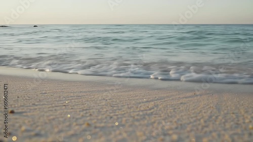Serene low angle footage of gentle ocean waves lapping onto a golden sandy beach during a calm and beautiful sunrise or sunset