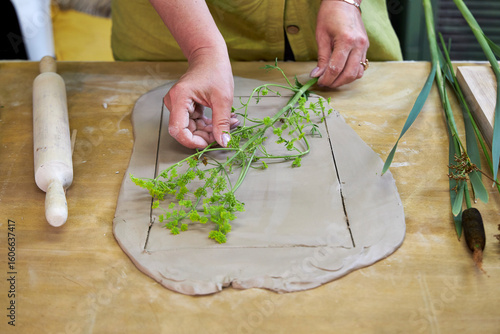 Placing fresh flowers and leaves on soft clay to create an imprint for plaster relief. Hands arranging botanical elements during DIY floral art tutorial in a step-by-step creative process