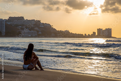 Chica joven sentada en la playa al amanecer