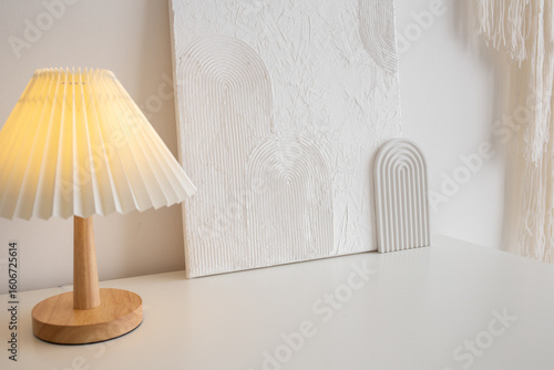 An on table lamp with a white corrugated shade and white trendy decor stand on chest of drawers. Home decor. Trendy white stylish interior.