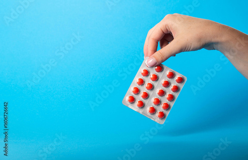 Foto Female hand holding blisters with red pills on blue background