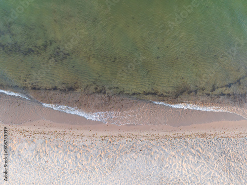 Fototapeta Naklejka Na Ścianę i Meble -  Serene aerial top-down view of the Baltic Sea coastline, with gentle transparent waves washing over the soft, sandy beach.