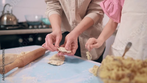 Mom and daughter cooking food. Little girl helps her mother prepare dinner. Family makes dumplings at home in the kitchen.