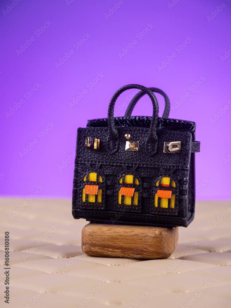 Obraz premium Close-up of a beautiful leather handbag with transparent windows for storing small items and wireless earbuds, set against a purple background