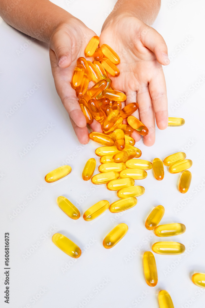 Child hands holding and pouring yellow soft gel capsules on white background Child hands holding and pouring yellow soft gel capsules on white background