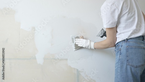 Unknown female construction worker applying plaster with putty knife, smoothing wall surface during home renovation, fixing wall imperfections with professional drywall repair technique, close up