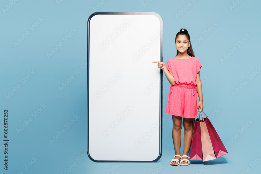 Little kid girl 9-10 years old wear pink clothes hold package bags after shopping point on big huge blank screen mobile cell phone isolated on plain blue background. Black Friday sale buy day concept. Little kid girl 9-10 years old wear pink clothes hold package bags after shopping point on big huge blank screen mobile cell phone isolated on plain blue background. Black Friday sale buy day concept.