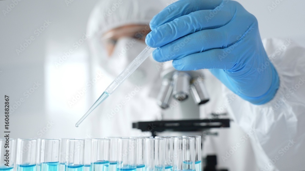 Fototapeta premium Scientific researcher wearing protective equipment, carefully pipetting liquid into test tubes while conducting medical research experiment. Medicine, healthcare and science concept