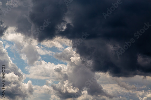 Tablou pe pânză Large dark clouds above cover light clouds below in the sky close-up, dark and white swirling clouds divide the sky, sharp weather change, cloudy background