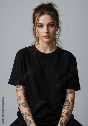 Studio portrait of a stylish young woman with arm tattoos wearing a black t-shirt