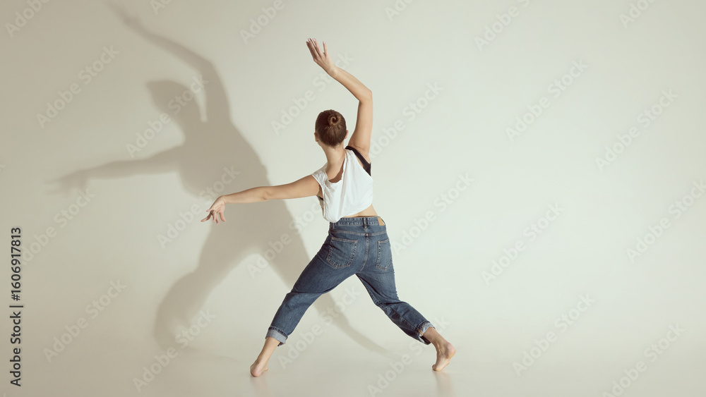 Fototapeta premium Inner voice. Young dancer captured from behind mid contemporary movement with dramatic shadow on wall. Concept of emotional expression, dance education visuals, motion capture and emotional awareness.