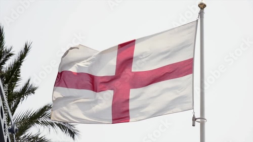 A static shot of the Flag of Saint George, white with a red cross, waving gently in the wind against a clear sky