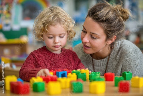 A kindergarten teacher helping a child with puzzles, both focusing on building blocks together in a playful and educational setting.