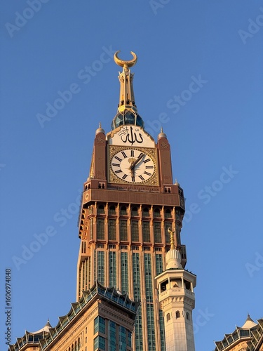 Abraj Al Bait Clock Tower in Mecca during sunset, with Islamic architecture and minarets under a clear blue sky, near the Grand Mosque