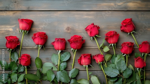 Roses Arranged on Wooden Surface Showcasing Vibrant Red Colors and Lush Green...