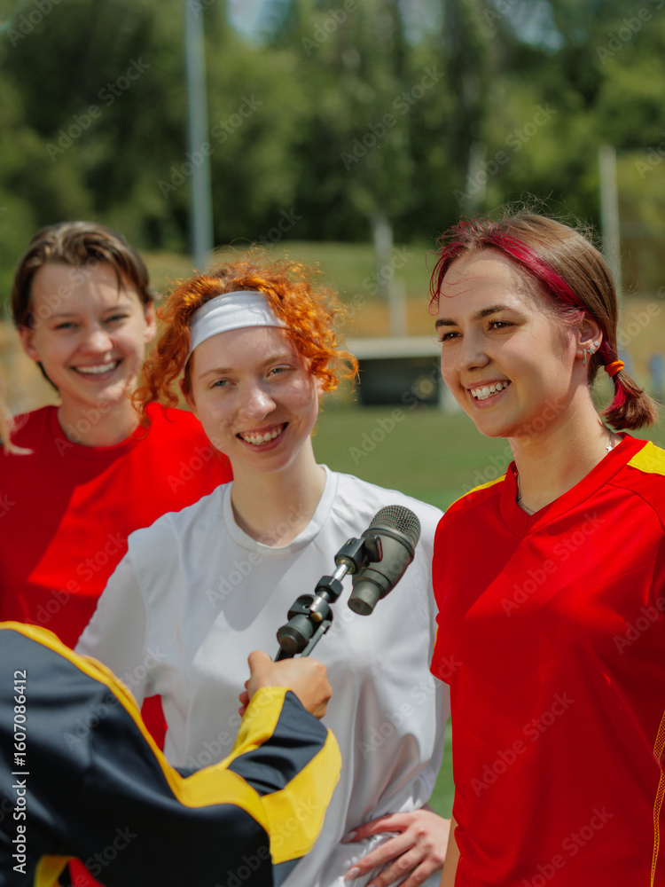 Naklejka premium Smiling female football players interviewed after game on sunny day. Concept of representation in media, diversity and sport coverage campaigns.