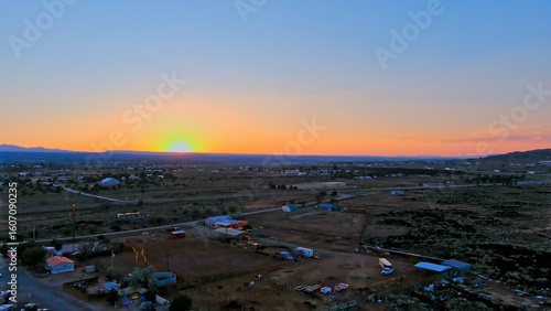 Aerial view of the Grants New Mexico landscape during sunset with a sprawling, semi-arid terrain. Sparse infrastructure includes low-lying buildings, roads, and some vegetation.