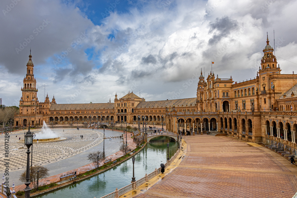 Fototapeta premium View of Plaza de España in Seville, Spain, taken from the South Tower, showing the entire structure including the canal and the North Tower on a partly cloudy day.