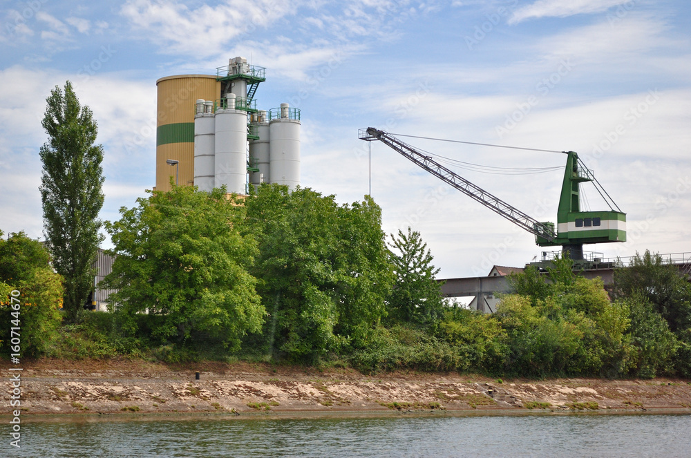 Fototapeta premium Riverside Industrial Site with Silos and Loading Crane 