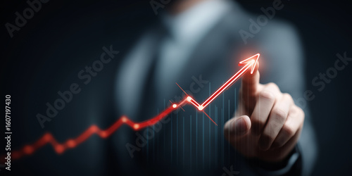 Person in suit is pointing at glowing red upward trend line on virtual graph, symbolizing business growth and success. background is dark, highlighting graph vibrant color